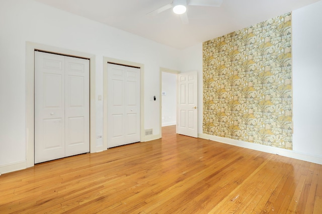 unfurnished bedroom with ceiling fan, wood-type flooring, and two closets