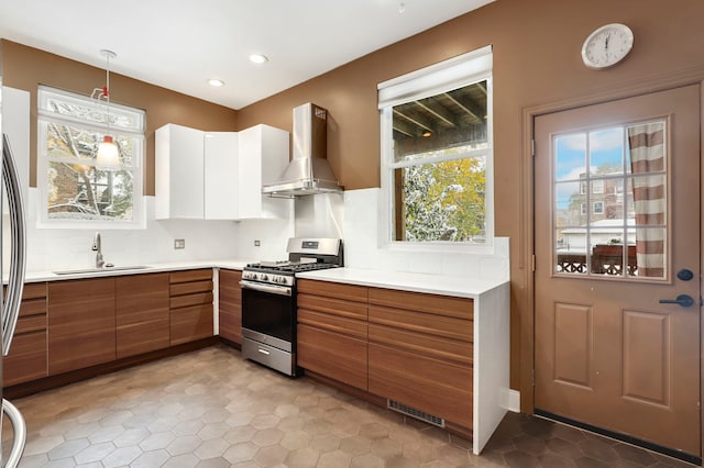 kitchen featuring appliances with stainless steel finishes, sink, wall chimney range hood, pendant lighting, and white cabinetry