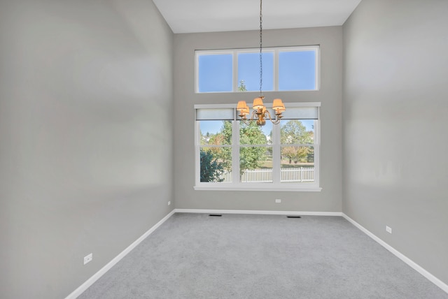 carpeted spare room with a notable chandelier and a towering ceiling