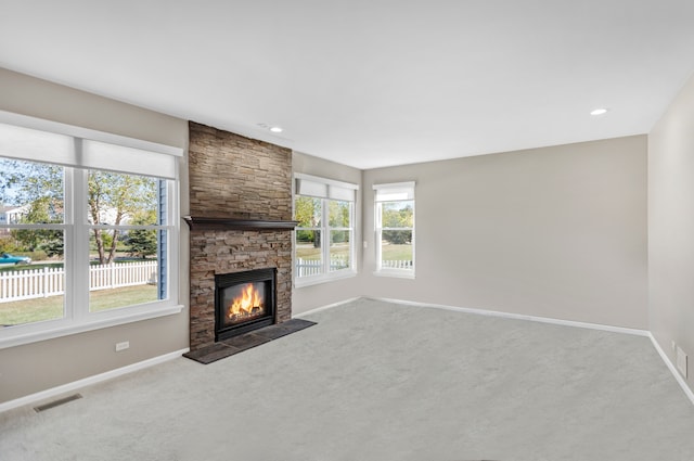 unfurnished living room featuring a stone fireplace, a healthy amount of sunlight, and carpet