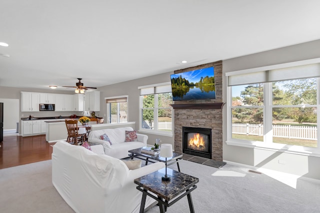 carpeted living room featuring a stone fireplace and ceiling fan