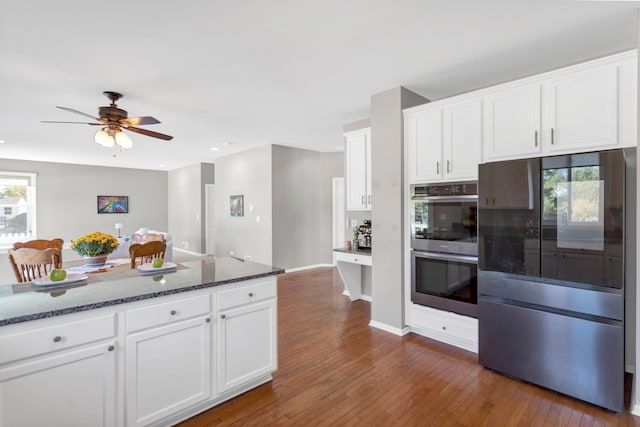 kitchen featuring white cabinets, dark wood-type flooring, dark stone counters, and double oven