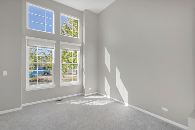 unfurnished room with carpet flooring, a towering ceiling, and a healthy amount of sunlight