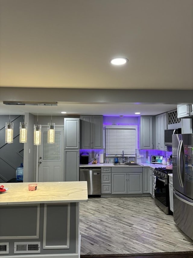 kitchen with gray cabinetry, sink, decorative light fixtures, appliances with stainless steel finishes, and light wood-type flooring