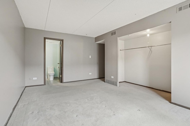 unfurnished bedroom featuring connected bathroom, a closet, and light carpet