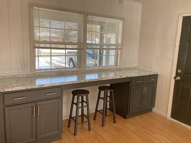 kitchen with light wood-type flooring, a kitchen bar, and light stone countertops