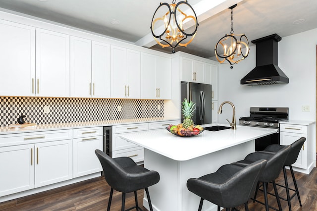 kitchen featuring stainless steel appliances, white cabinetry, hanging light fixtures, wall chimney exhaust hood, and a kitchen island with sink