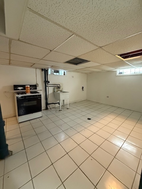 basement featuring a drop ceiling, sink, and light tile patterned floors