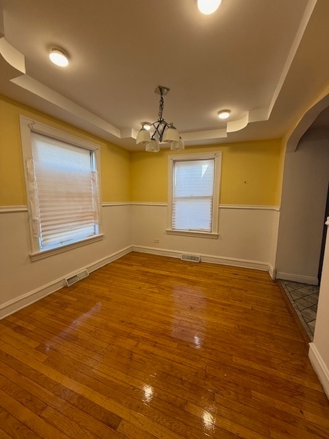 empty room featuring hardwood / wood-style flooring, an inviting chandelier, and a tray ceiling