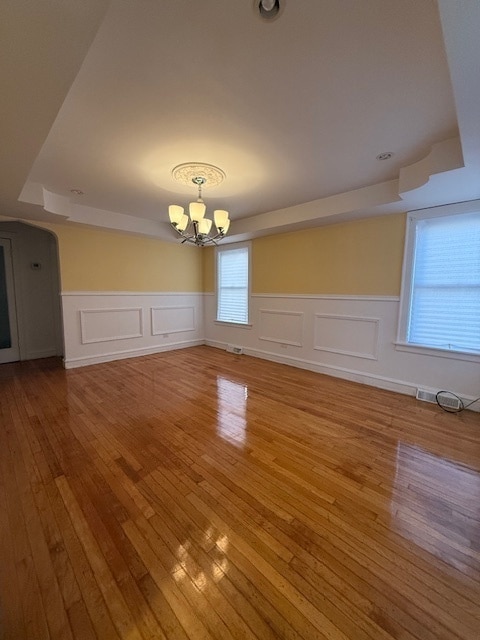 unfurnished dining area with hardwood / wood-style flooring, a raised ceiling, and an inviting chandelier