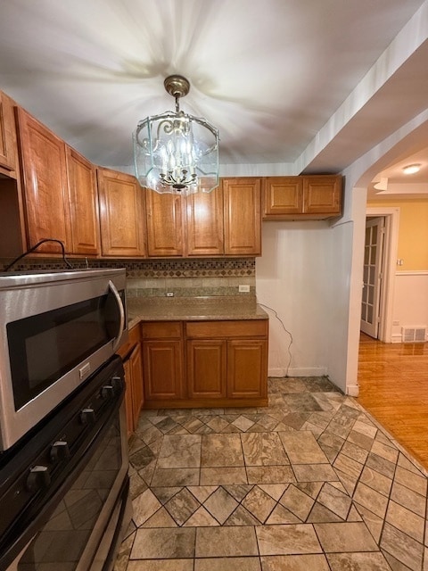 kitchen with light hardwood / wood-style floors, decorative backsplash, a notable chandelier, appliances with stainless steel finishes, and decorative light fixtures