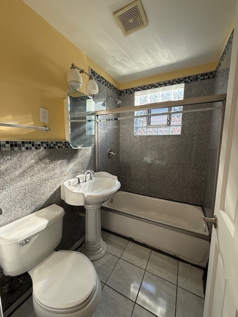 bathroom featuring tile patterned floors, toilet, tile walls, and tiled shower / bath combo