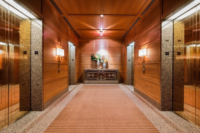 corridor with wood ceiling, elevator, wood walls, and light colored carpet