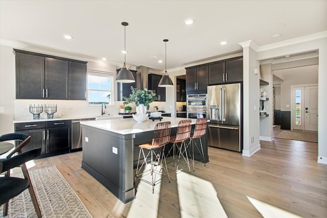 kitchen with a kitchen bar, light hardwood / wood-style flooring, a kitchen island, pendant lighting, and appliances with stainless steel finishes