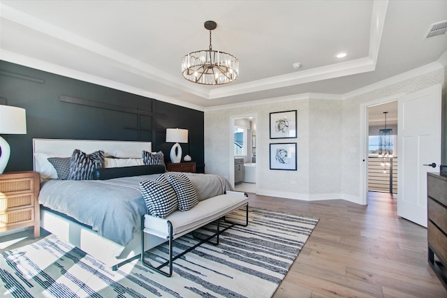 bedroom featuring a raised ceiling, wood-type flooring, a notable chandelier, and ensuite bathroom