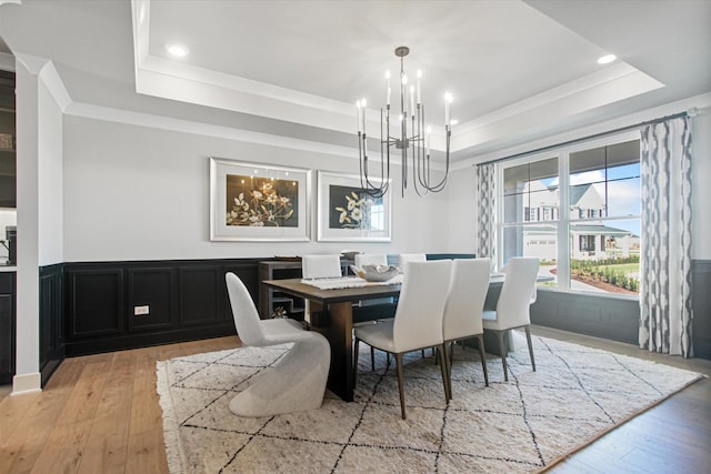 dining area with light wood-type flooring, a chandelier, and a raised ceiling