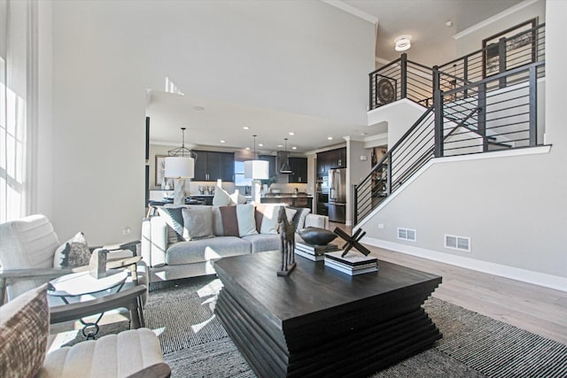 living room with hardwood / wood-style flooring, a towering ceiling, and ornamental molding