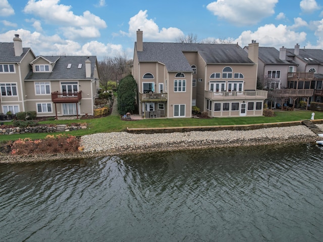 back of property with a lawn, a sunroom, a balcony, and a water view