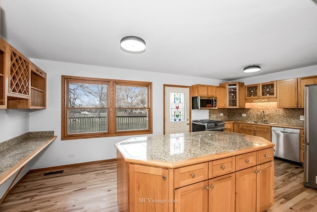 kitchen featuring light wood-type flooring, backsplash, stainless steel appliances, sink, and a center island