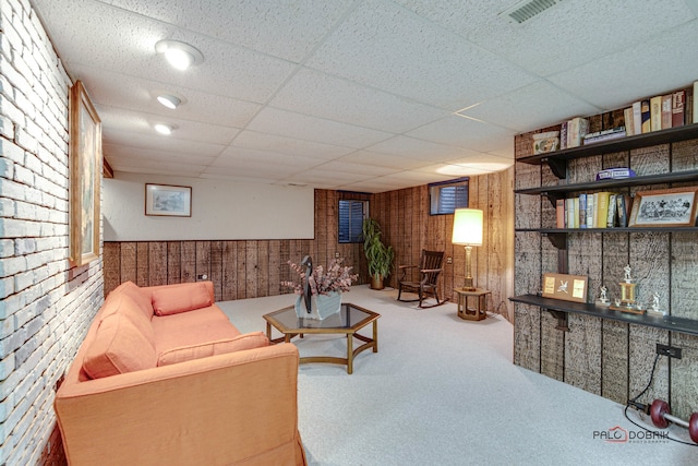 living room featuring a paneled ceiling, brick wall, carpet floors, and wooden walls