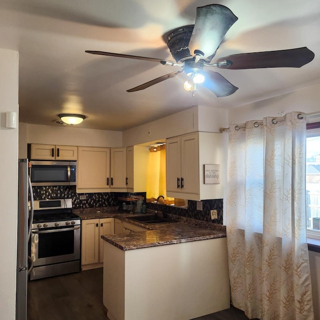 kitchen featuring sink, appliances with stainless steel finishes, kitchen peninsula, dark stone counters, and backsplash