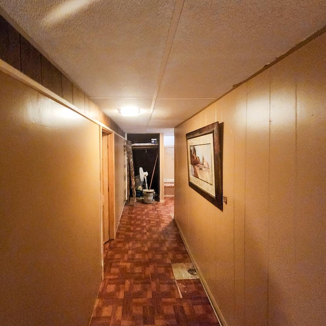 hallway featuring dark parquet flooring, a textured ceiling, and wood walls