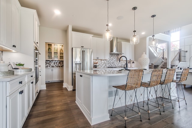 kitchen with dark wood-type flooring, white cabinets, hanging light fixtures, wall chimney range hood, and a breakfast bar