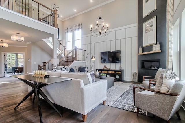 living room with a fireplace, crown molding, a towering ceiling, a notable chandelier, and hardwood / wood-style flooring