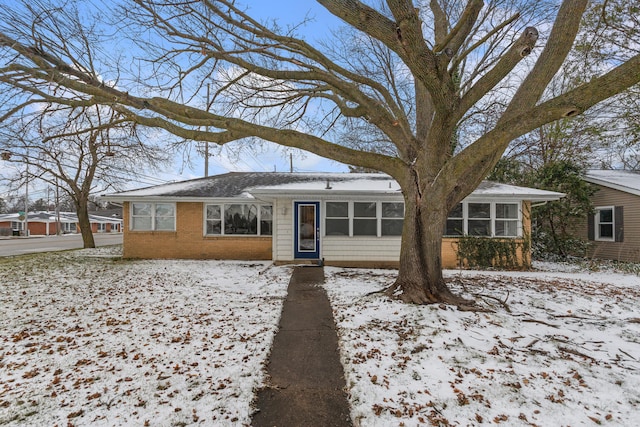 snow covered back of property featuring a sunroom