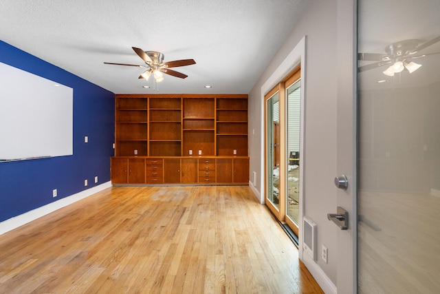 unfurnished room featuring built in shelves, a textured ceiling, and light wood-type flooring