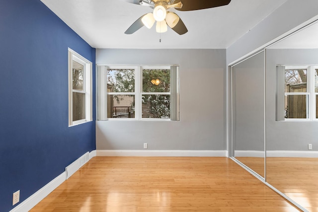 unfurnished bedroom with ceiling fan, light hardwood / wood-style flooring, multiple windows, and a closet