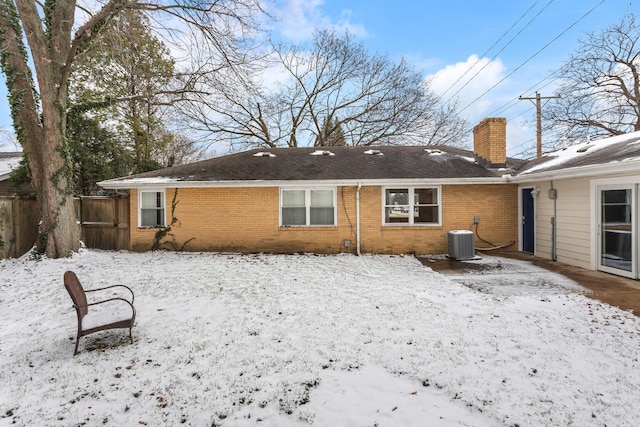 snow covered rear of property featuring central AC unit