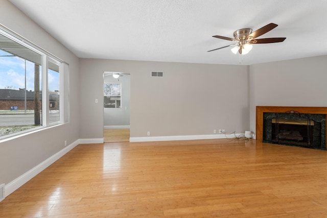 unfurnished living room featuring ceiling fan, light hardwood / wood-style flooring, a high end fireplace, and a textured ceiling