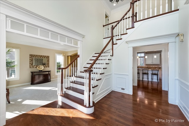 stairs with crown molding, a decorative wall, a towering ceiling, and wood finished floors