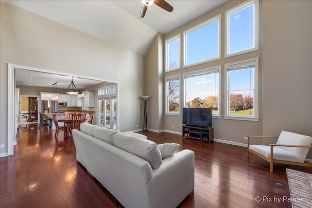 living area featuring high vaulted ceiling, dark wood-type flooring, a ceiling fan, and baseboards