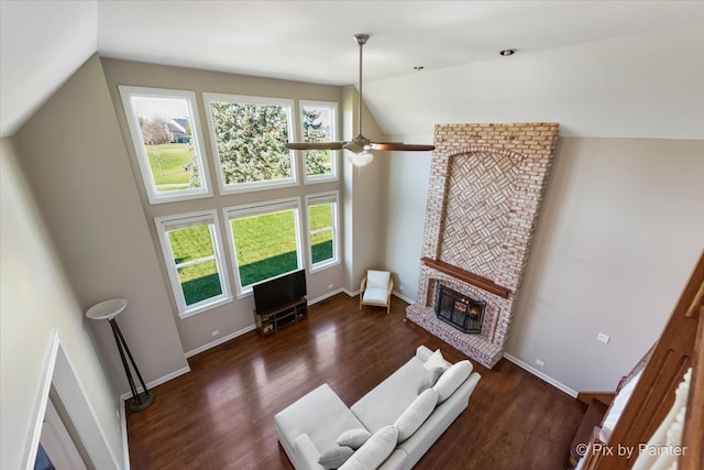 living room with high vaulted ceiling, a fireplace, baseboards, and wood finished floors