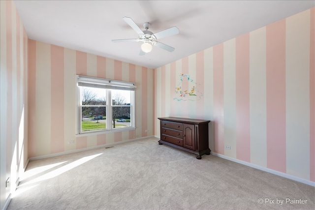 carpeted empty room featuring wallpapered walls, baseboards, and a ceiling fan