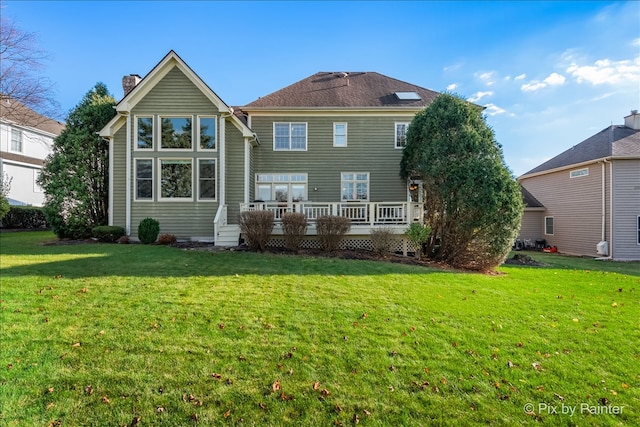 rear view of house featuring a chimney, a lawn, and a wooden deck