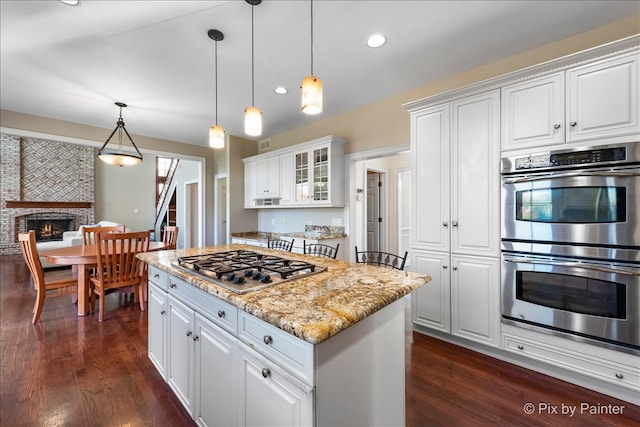 kitchen featuring dark wood-style flooring, white cabinetry, hanging light fixtures, appliances with stainless steel finishes, and a brick fireplace