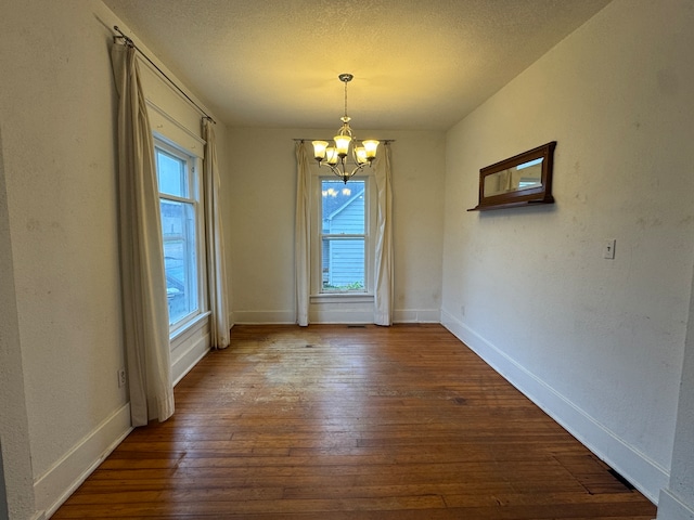 unfurnished dining area featuring hardwood / wood-style flooring, a notable chandelier, and a textured ceiling