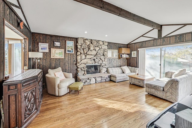 living room with vaulted ceiling with beams, wood walls, light hardwood / wood-style flooring, and a stone fireplace