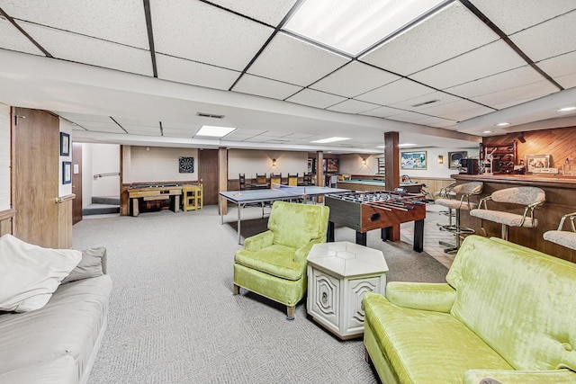 recreation room with a drop ceiling, light colored carpet, bar, and wood walls