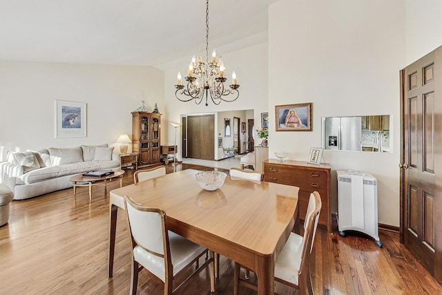 dining room featuring wood-type flooring, high vaulted ceiling, and an inviting chandelier