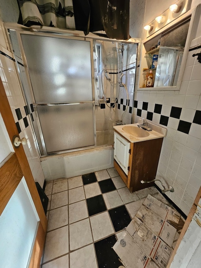 bathroom with bath / shower combo with glass door, vanity, and tile walls