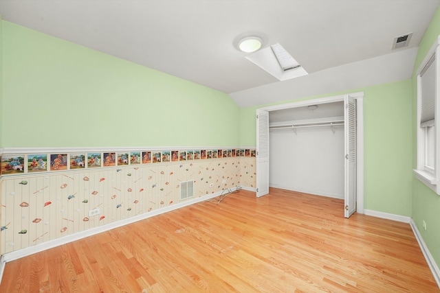 unfurnished bedroom with a closet, a skylight, and hardwood / wood-style flooring