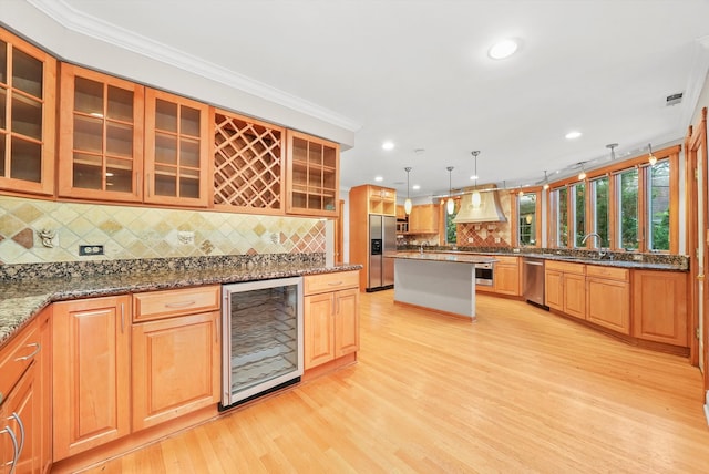 kitchen with light hardwood / wood-style floors, appliances with stainless steel finishes, dark stone counters, beverage cooler, and crown molding