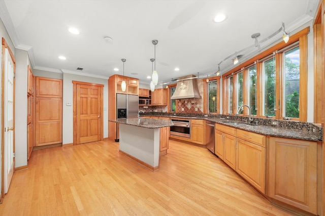 kitchen featuring light hardwood / wood-style floors, appliances with stainless steel finishes, hanging light fixtures, a kitchen island, and wall chimney range hood