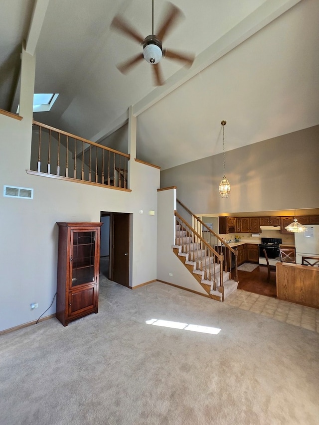 unfurnished living room featuring ceiling fan, a skylight, high vaulted ceiling, and carpet floors