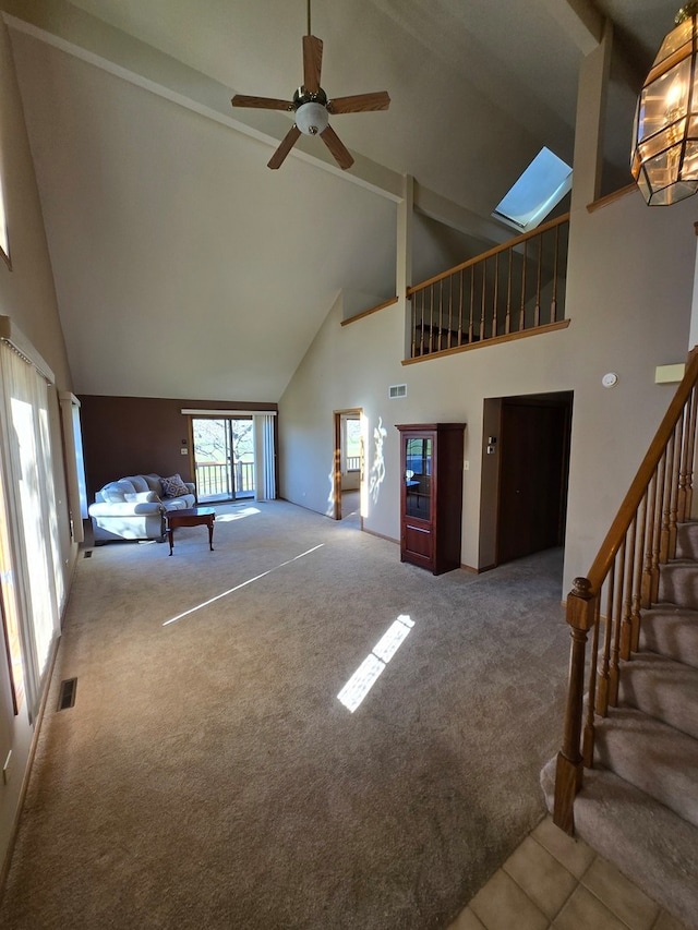 unfurnished living room featuring high vaulted ceiling, a skylight, carpet, and ceiling fan