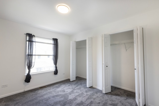 unfurnished bedroom with multiple closets and dark carpet